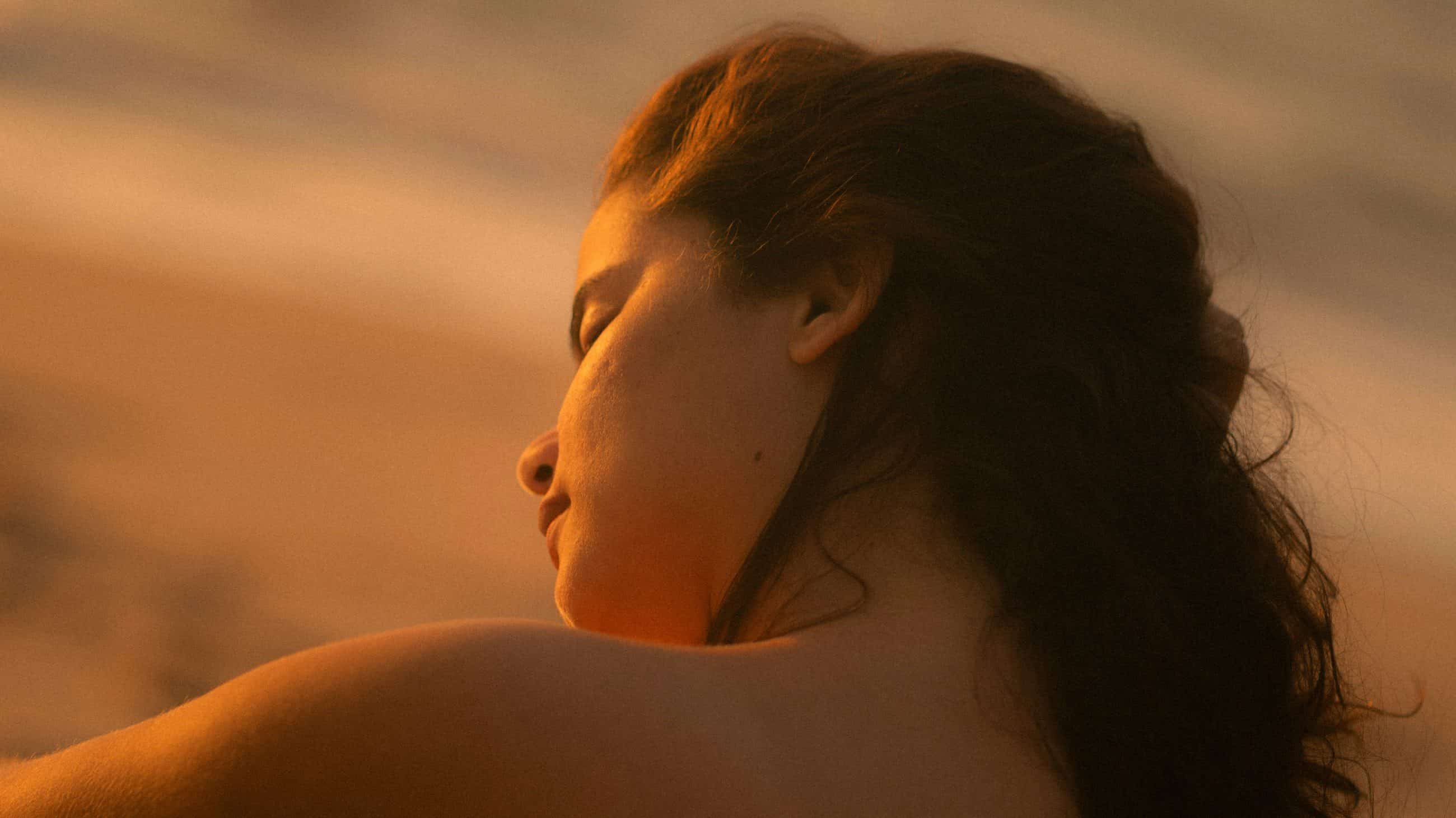 Mujer con los ojos cerrados bajo una luz cálida, expresión serena